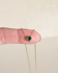 Gold necklace with a green gemstone held between fingers on a beige background