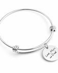 A silver-toned metal expandable wire bangle bracelet with a round engraved disc charm that reads 'Love, Mom and Dad' on a clean white background.