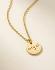 Gold necklace with a round pendant inscribed with the word 'angel' on a beige background
