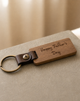 Wooden keychain with leather strap and 'Happy Father's Day' engraving on a neutral background
