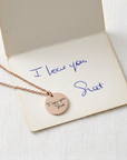 Necklace with a round pendant on a card with 'I love you' written on it, on a light background