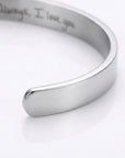 A polished silver-toned metal cuff bracelet with engraved text inside, shown on a clean white background.