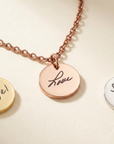 Rose gold necklace with engraved disc pendants on a beige background