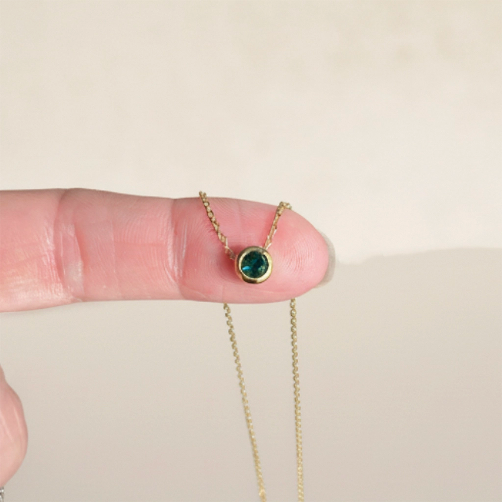 Gold necklace with a green gemstone held between fingers on a beige background