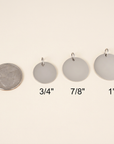 Set of four round metal handwriting pendants with measurements on a beige background