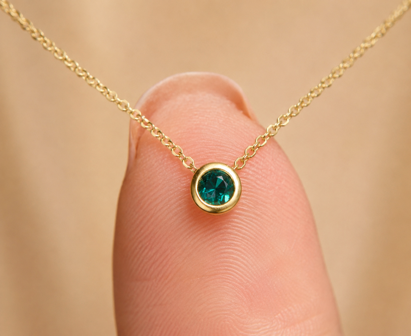 Gold necklace with a green gemstone held on finger for scale on beige background