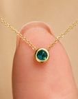 Gold necklace with a green gemstone held on finger for scale on beige background