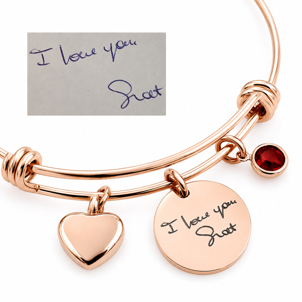 Rose gold double-band expandable bracelet with a heart charm, a round disc charm engraved with 'I love you Shot', a small red gemstone charm, and a small inset showing a handwritten note that reads 'I love you Shot'.
