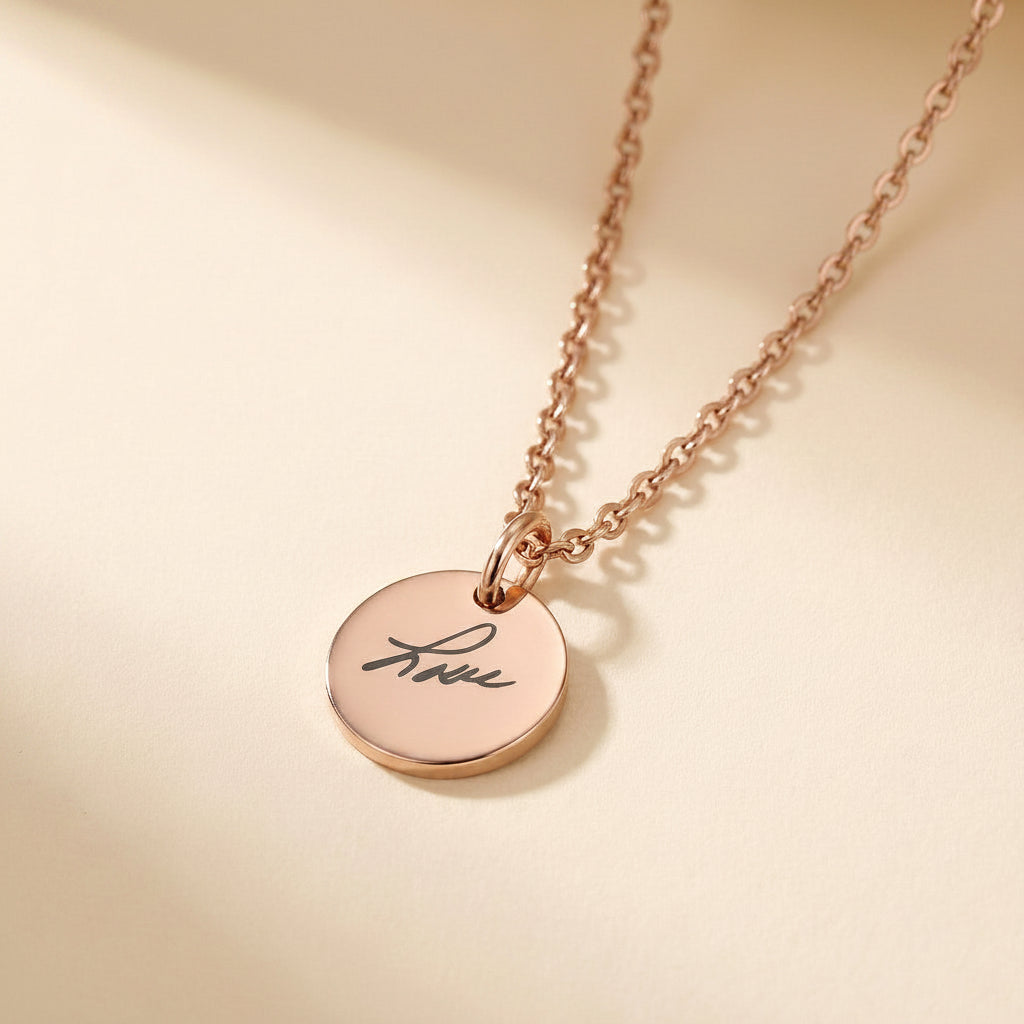 Rose gold necklace with a round pendant engraved with 'love' on a beige background