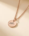 Rose gold necklace with a round pendant engraved with 'love' on a beige background