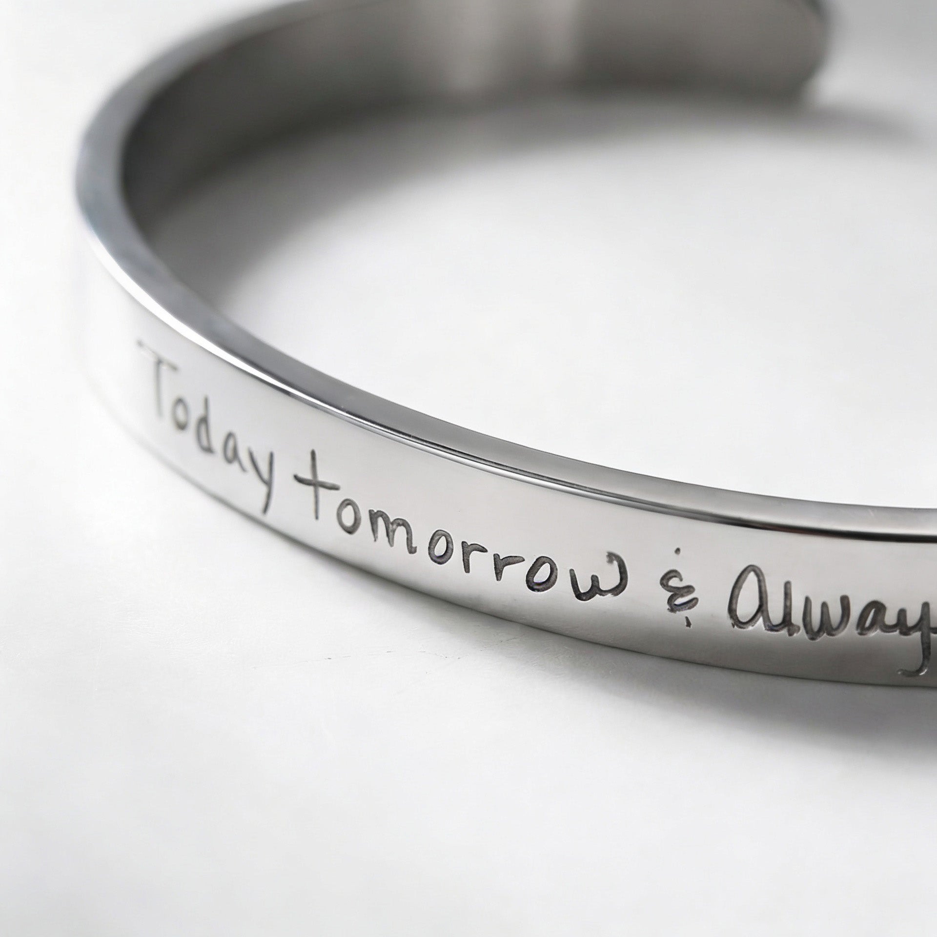 A close-up of a polished silver cuff bracelet engraved with the handwritten phrase 'Today tomorrow &amp; Always'.
