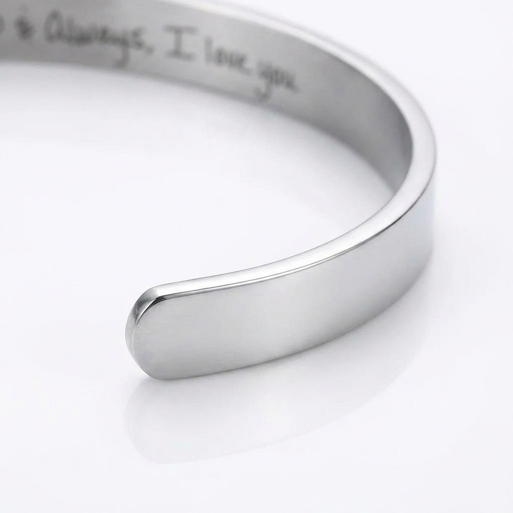 A polished silver-toned metal cuff bracelet with engraved text inside, shown on a clean white background.