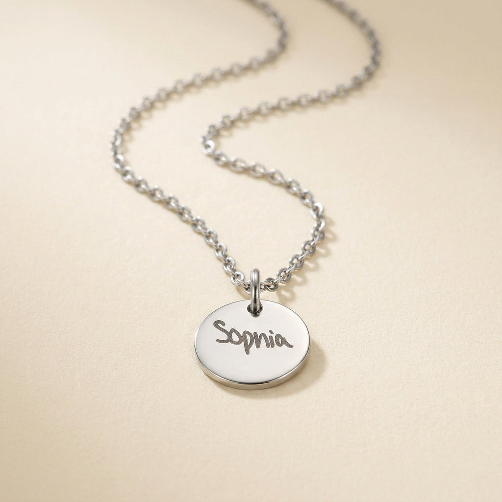 Silver necklace with a round pendant engraved with 'Sophia' on a beige background