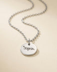 Silver necklace with a round pendant engraved with 'Sophia' on a beige background