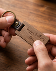 Wooden keychain with 'Happy Father's Day' engraving held by hands on a wooden surface